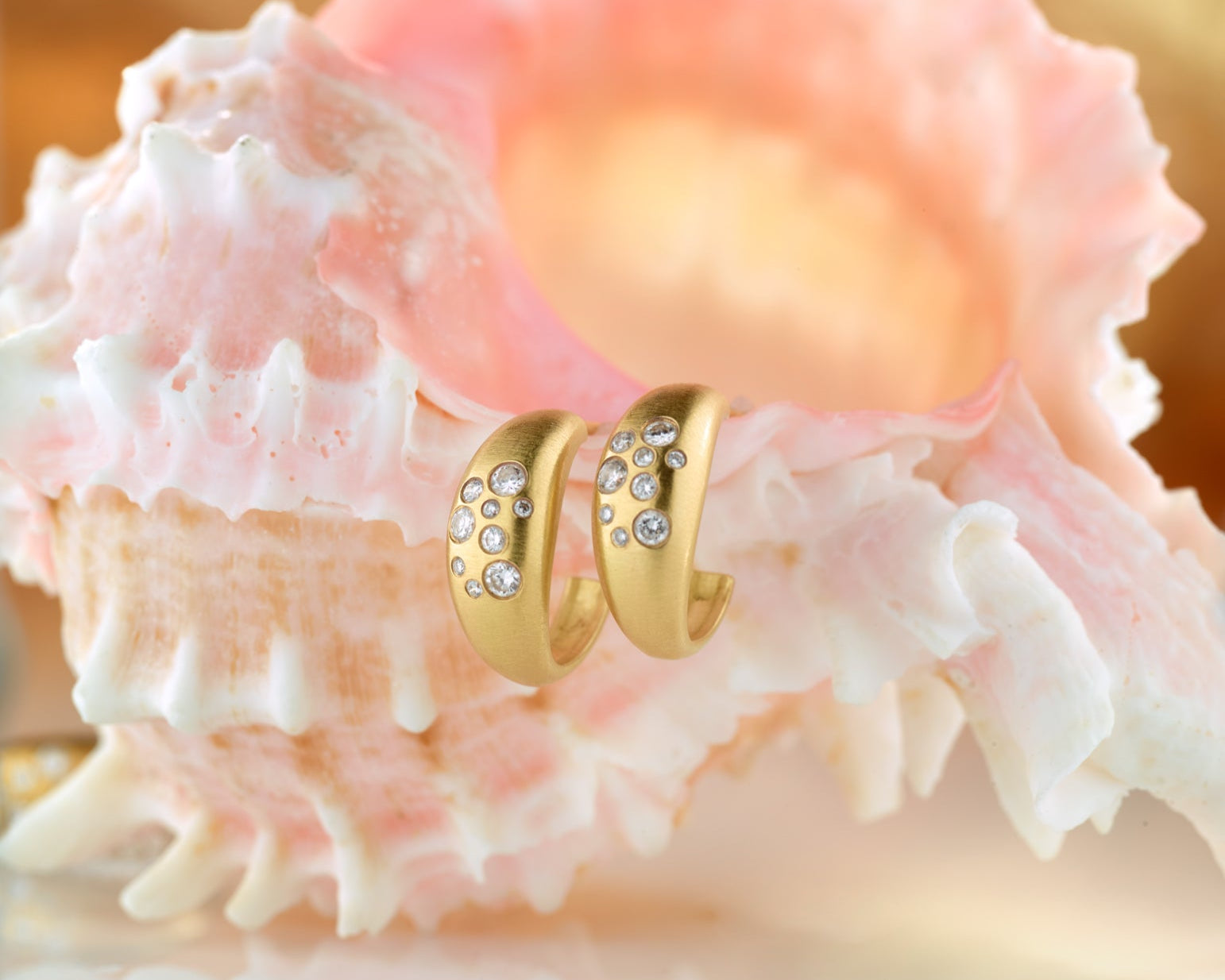 Gold ring with gemstones on a pink shell against a blurred background